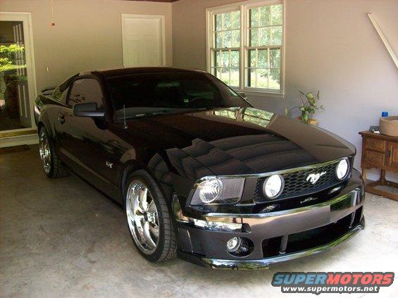 Black Ford Mustang parked in a garage, front 3/4 view. Chrome wheels and grille