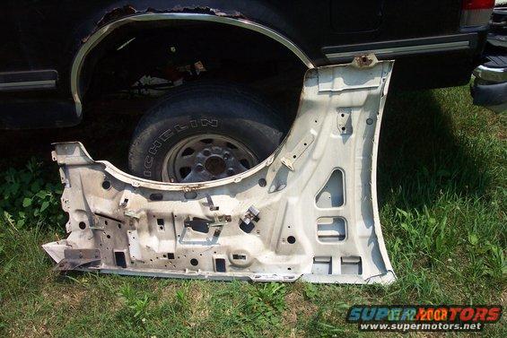 Disassembled vehicle door lying on grass next to a rusty wheel well