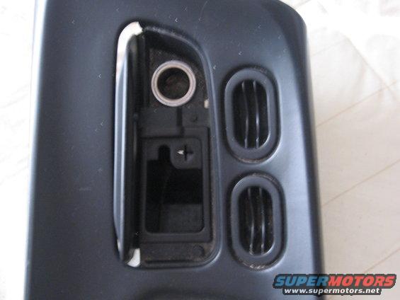 Dark gray car interior part with two oval air vents and a circular opening above a rectangular compartment