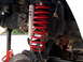 1996 Ford Bronco - Close-up view of a vehicle's front suspension system, showing a red coil spring and a shock absorber.