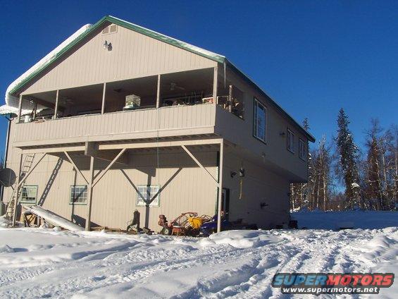 House with snow on the roof and ground, some equipment visible near the foundation