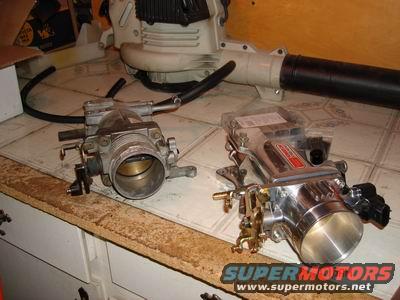 Two throttle bodies on a counter, one is chrome and has a red label