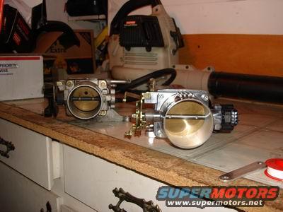 Two throttle bodies on a workbench, one shiny, one matte