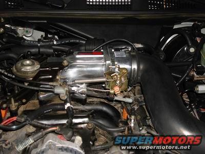 Engine bay with chrome intake manifold, black hoses, and wiring. Supermotors.net logo visible