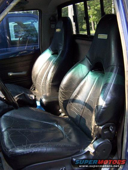 Black leather bucket seats with Momo logos inside a blue truck cab, showing wear and tear