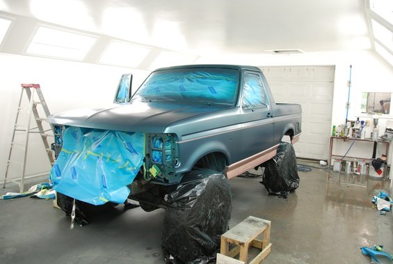 Ford truck covered in blue plastic and tape in a garage, prepped for painting. Doors are open