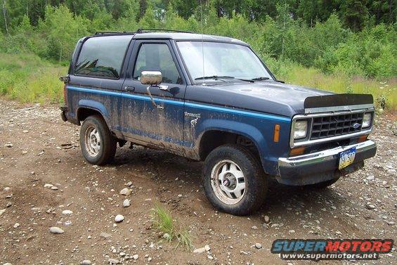 Blue 1989 Ford Bronco II parked on a dirt road, covered in mud