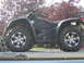 2008 Honda RANCHER - A black four-wheel ATV with custom wheels is parked on a trailer, with trees and a house in the background.