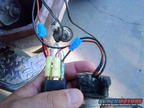 Hand holding automotive relay and wiring harness with blue and yellow connectors