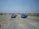 1985 Ford Mustang - Two cars, a blue Subaru WRX and a black Mazda Miata, are lined up on a race track with cones marking the course.