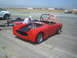 1985 Ford Mustang - A man works on the engine of a red convertible sports car parked on an asphalt surface, possibly an airfield.