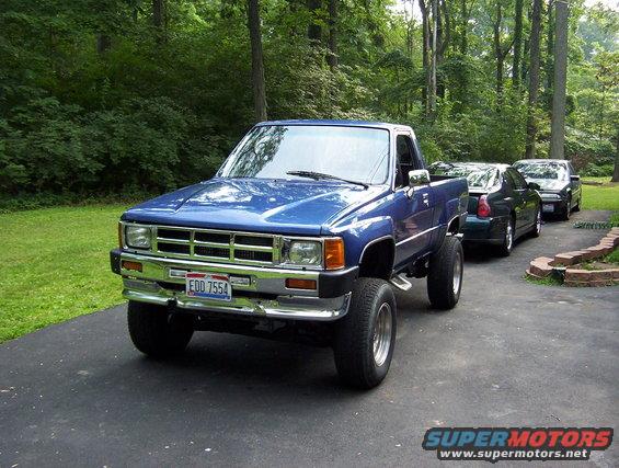 Blue pickup truck with chrome bumper and grille, lifted suspension, and aftermarket wheels