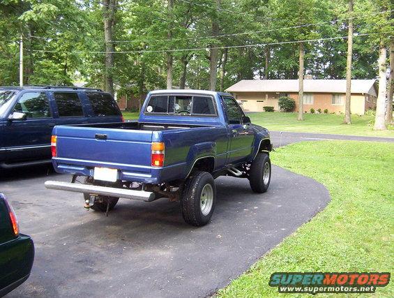 1986 Toyota Hilux pickup truck parked in driveway, rear view. Another SUV is parked to the left
