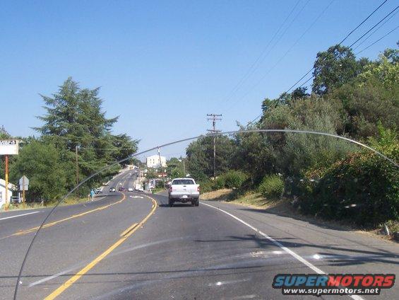 White pickup truck from the rear, driving on a two-lane road with trees and power lines. The truck appears to be from the early to mid-1990s
