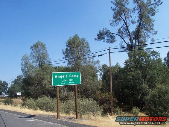 Sign says Angels Camp City Limit. Trees and power lines in background