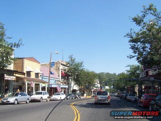 Street view of a town with parked cars and buildings under a clear blue sky