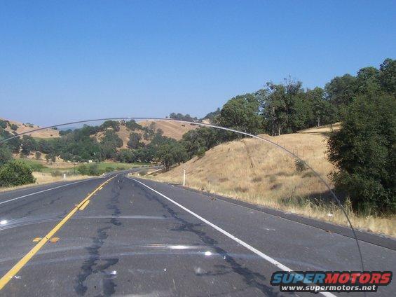 View from car on highway with rolling hills and trees under a clear blue sky