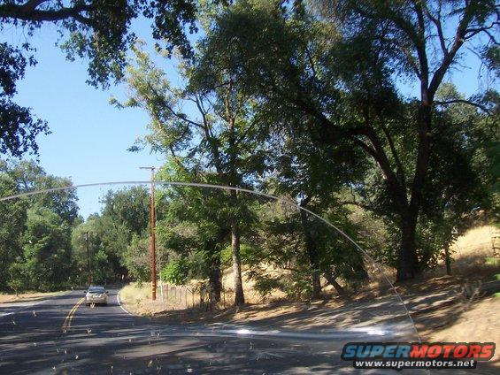 Car driving on a two-lane road with trees and a fence on the side