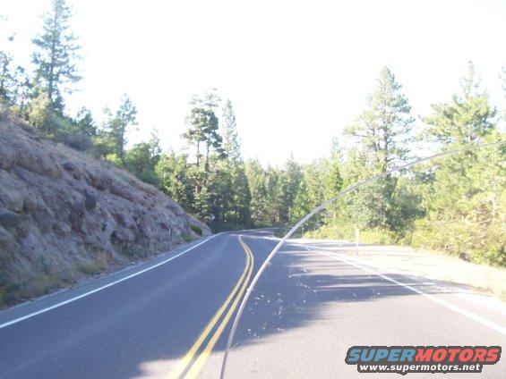 Winding asphalt road with double yellow lines passes through a wooded area with a rocky embankment