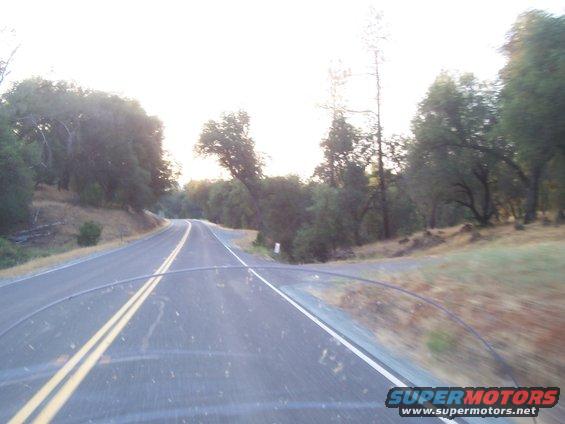 Windshield view of a two-lane road through a wooded area