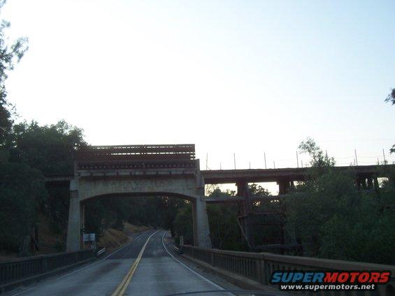 Driving on a road under two bridges, one concrete arch and one older railway bridge
