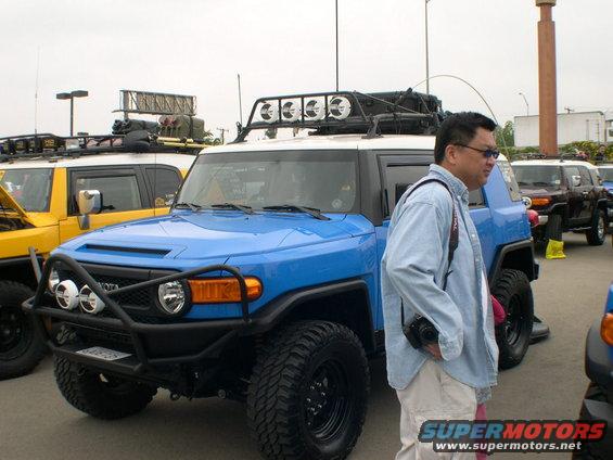 Blue Toyota FJ Cruiser with roof rack and aftermarket bumper. Yellow FJ Cruiser in background