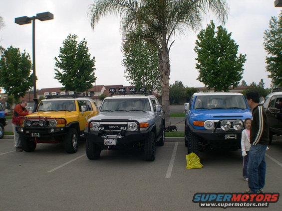 Three Toyota FJ Cruisers parked in a lot, one yellow, one silver, one blue