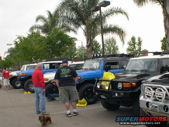 Several Toyota FJ Cruisers parked in a lot. People are standing around them