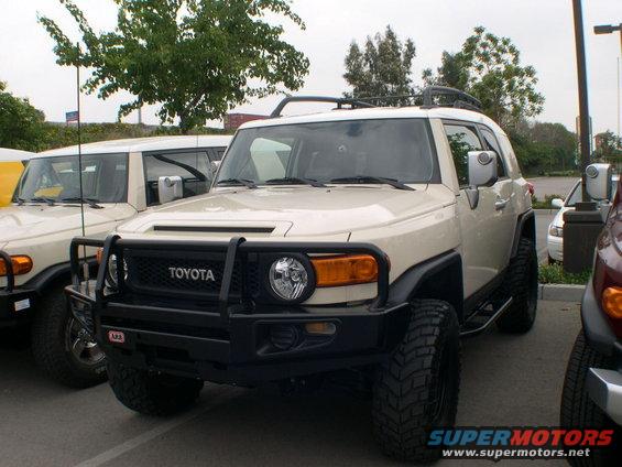 Front view of a tan 2007 Toyota FJ Cruiser with a black bull bar and another FJ Cruiser behind it