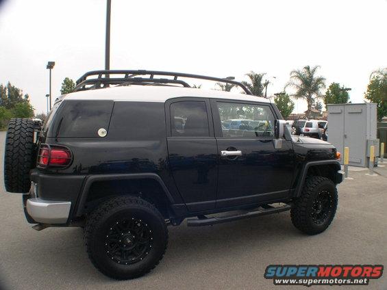 Black Toyota FJ Cruiser with white roof, spare tire on rear, aftermarket wheels, and roof rack