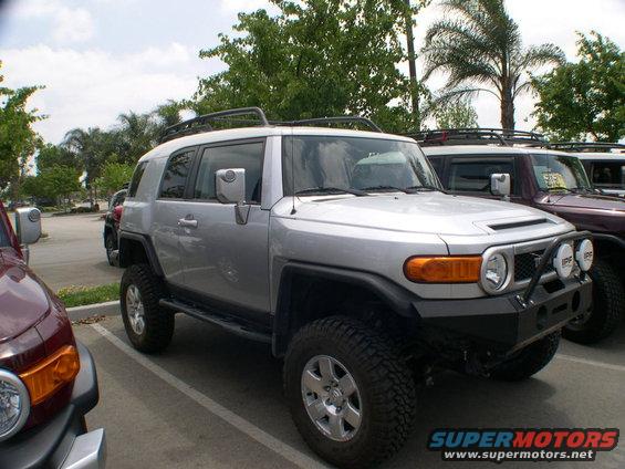 Silver Toyota FJ Cruiser parked next to a maroon one. Aftermarket bumper and lights visible