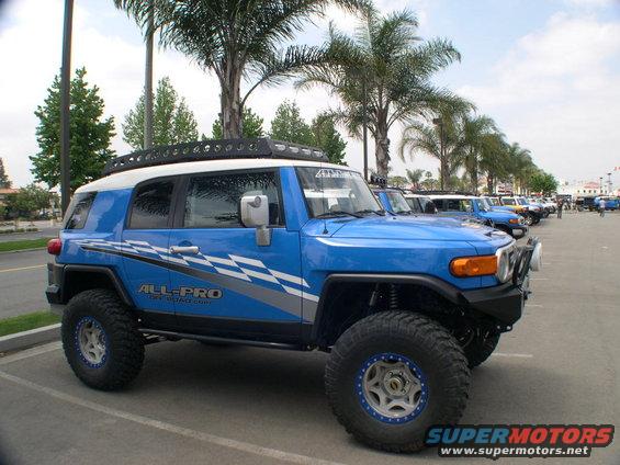 Blue Toyota FJ Cruiser with white roof, off-road tires, and 'ALL-PRO' graphics parked in a lot
