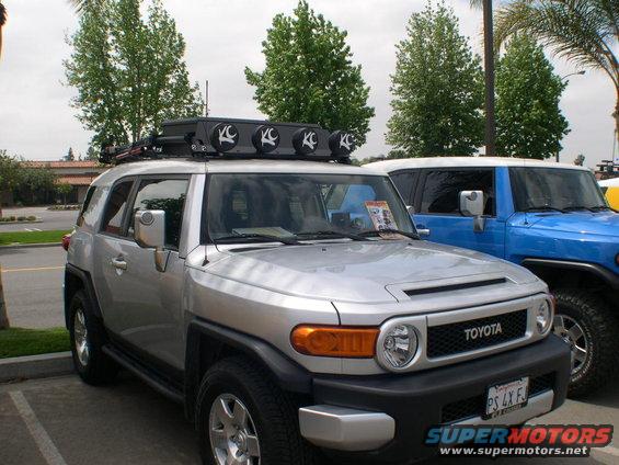 Silver 2007 Toyota FJ Cruiser with KC lights on roof rack, parked next to a blue FJ Cruiser
