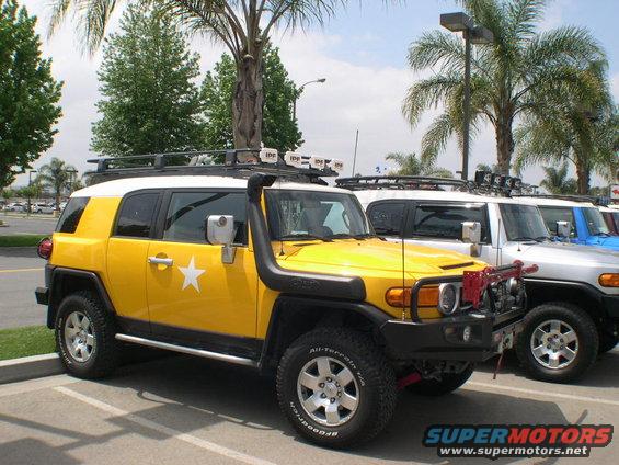 Yellow Toyota FJ Cruiser with snorkel and roof lights, parked next to other FJ Cruisers