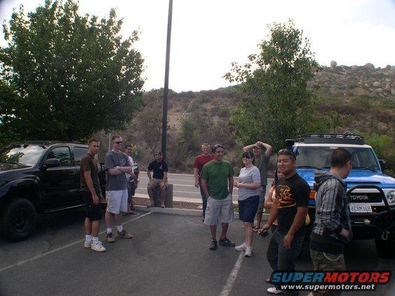 Blue Toyota FJ Cruiser with roof rack and black Toyota Tacoma parked in a lot with people