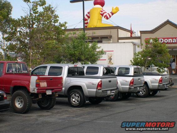 Several silver Toyota Tacoma pickup trucks parked in a lot, with a red Toyota pickup in the foreground. Ronald McDonald inflatable is visible above a building