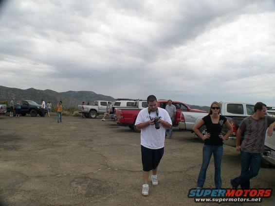 Several pickup trucks parked in a lot with people around. One guy is holding a camera