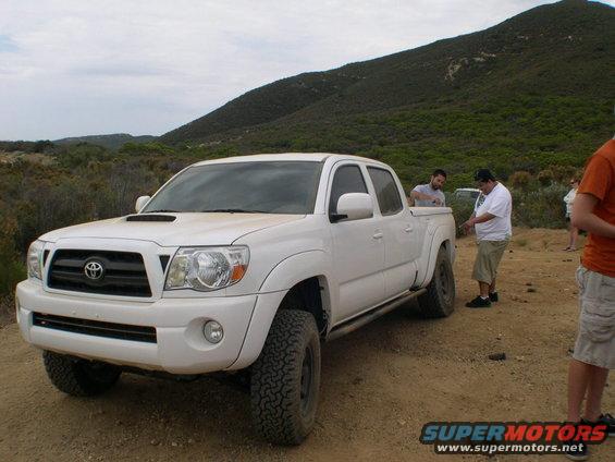 White Toyota Tacoma pickup truck, 3/4 front view. Hood scoop and off-road tires visible