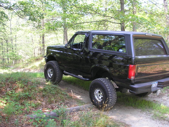 Black 1995 Ford Bronco with lifted suspension and off-road tires on a dirt path