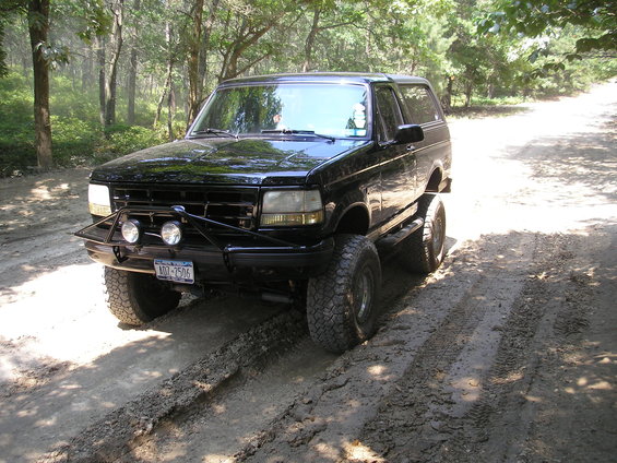 1995 Ford Bronco with aftermarket bumper and lights on a muddy dirt road