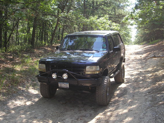 Black Ford Bronco with aftermarket bumper and off-road tires parked on a dirt road
