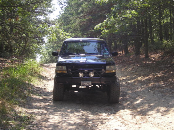 1995 Ford Bronco on a dirt road in a wooded area. Front view