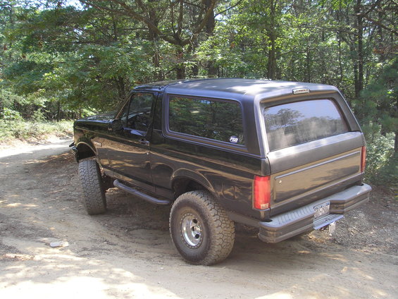 Black 1995 Ford Bronco parked on a dirt road with trees in the background