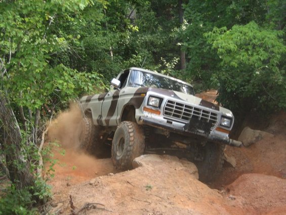 Camouflaged 1979 Ford F-150 climbing a dirt hill, kicking up dust