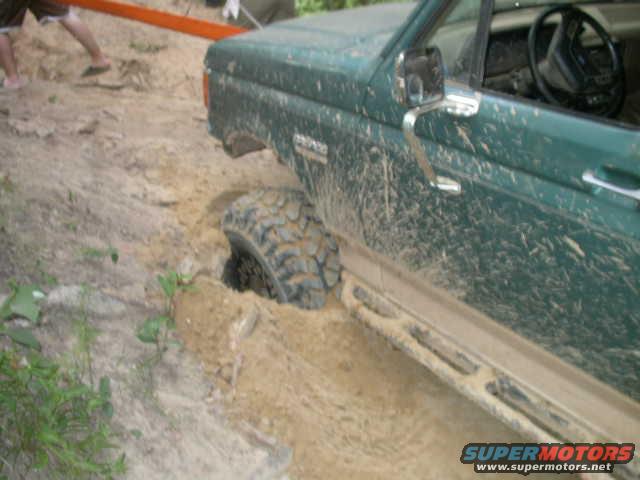 Green 1990 Ford Bronco stuck in mud, side view showing front wheel deep in dirt and side step