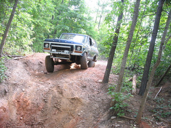 Blue 1978 Ford Bronco climbing a dirt hill on a wooded trail
