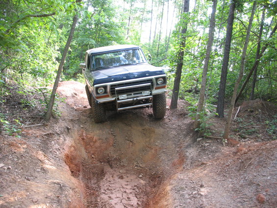 1978 Ford Bronco driving on a dirt trail through woods