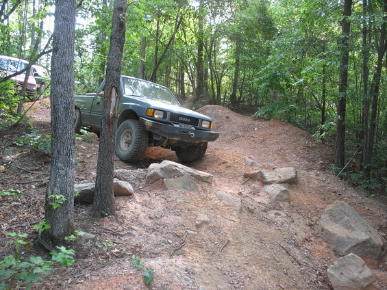 Green Isuzu pickup truck on a dirt trail with another vehicle behind it