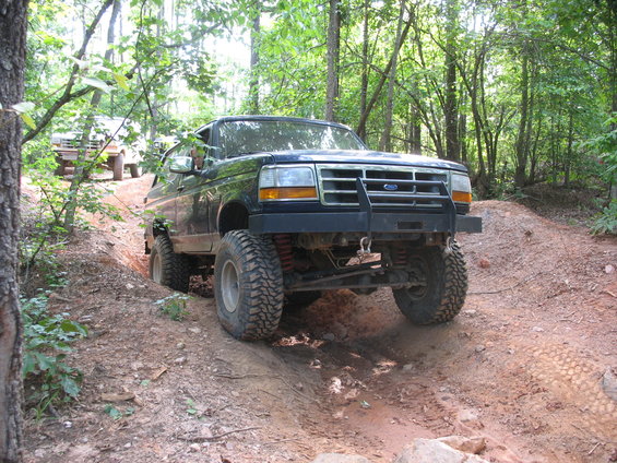 Dark blue Ford Bronco with a bull bar driving on a dirt trail