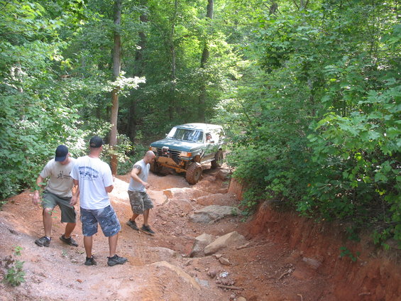 Green off-road SUV climbing a steep, rocky trail with three men watching